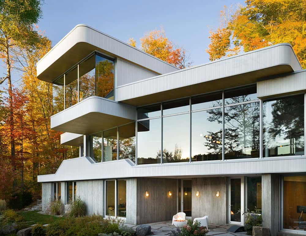 Close-up of multi-level contemporary home facade with floor-to-ceiling windows and curved white rooflines amid fall foliage