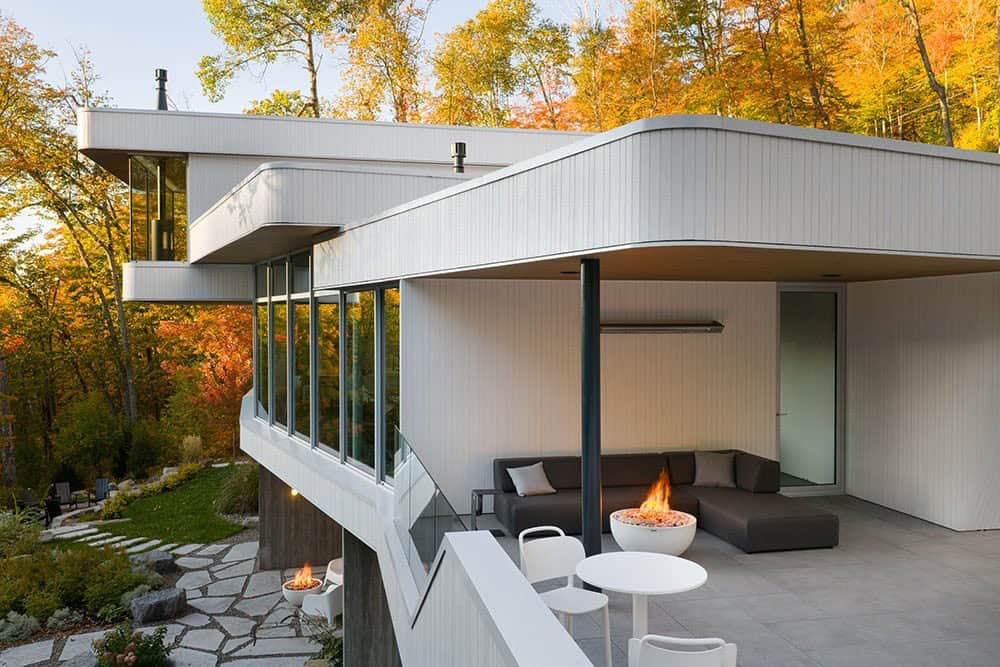 Covered outdoor terrace with dark sectional sofa and round fire pit bowl overlooking autumn forest