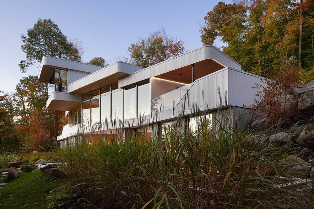 Side view of modern white home with expansive glazed walls and wood soffit detail at dusk