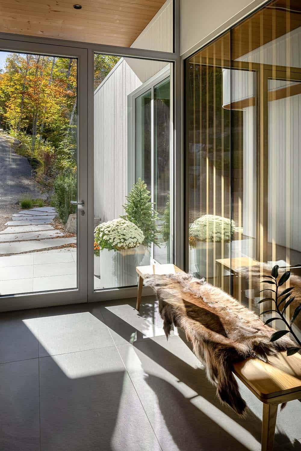 Sunlit entry foyer with large glass doors, fur-draped bench, and reflective glass partition