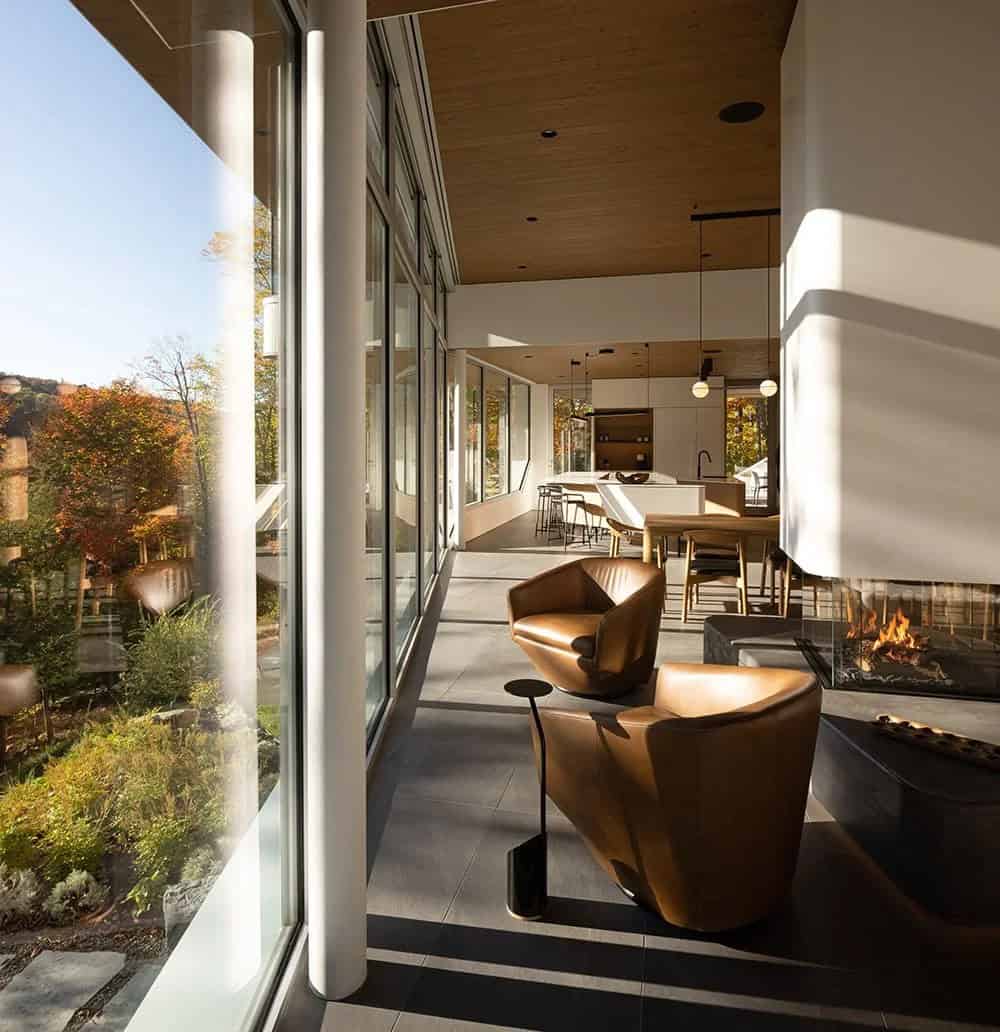 Interior view along glazed wall showing leather armchairs by fireplace with kitchen and dining area beyond