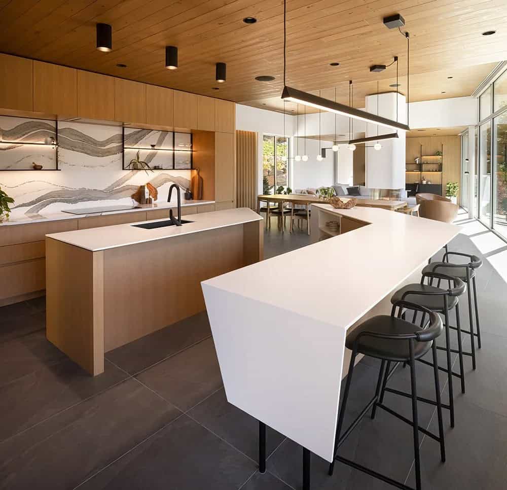 Spacious open-plan kitchen with white breakfast bar, wood cabinetry, dramatic backsplash, and living area beyond