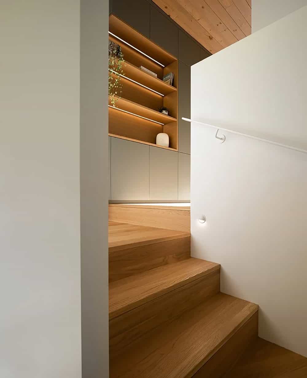 Wood staircase with backlit built-in shelving, white handrail, and warm pine ceiling