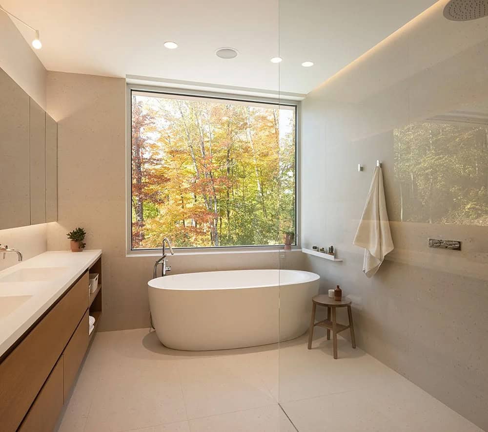 Primary ensuite with freestanding soaker tub, floor-to-ceiling forest window, and walk-in shower