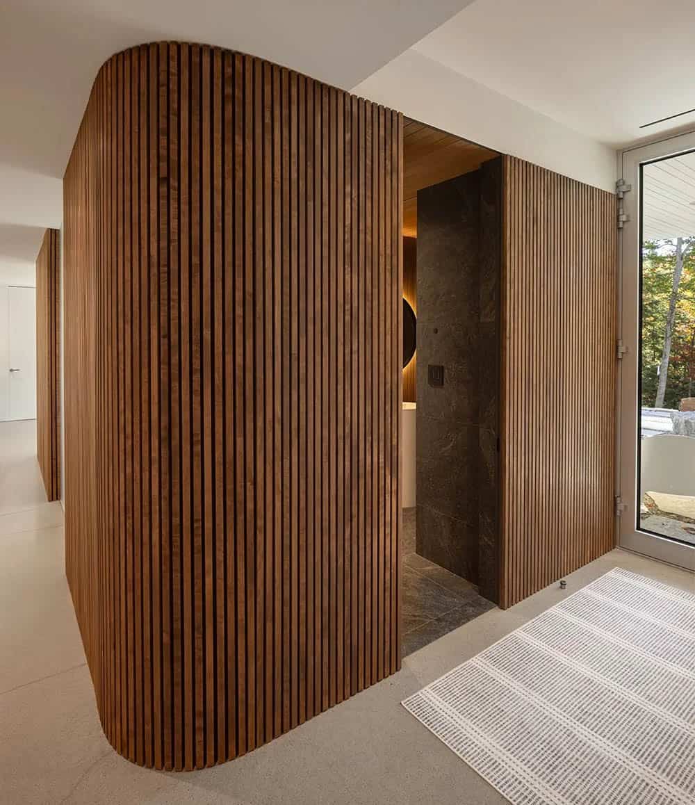 Curved vertical wood slat partition wall enclosing lower-level spa bathroom entrance