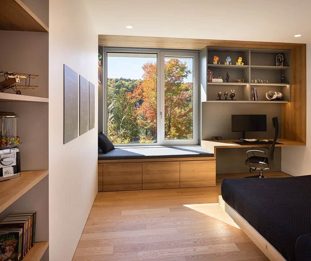 Kids bedroom with built-in window seat, integrated desk, open shelving, and autumn forest views