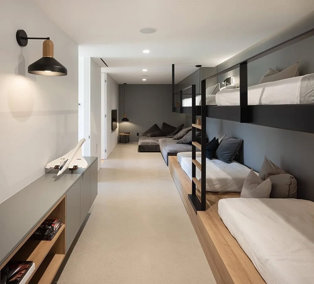 Long kids bunkroom with custom steel-framed double bunk beds, grey lounge seating, and wall sconces
