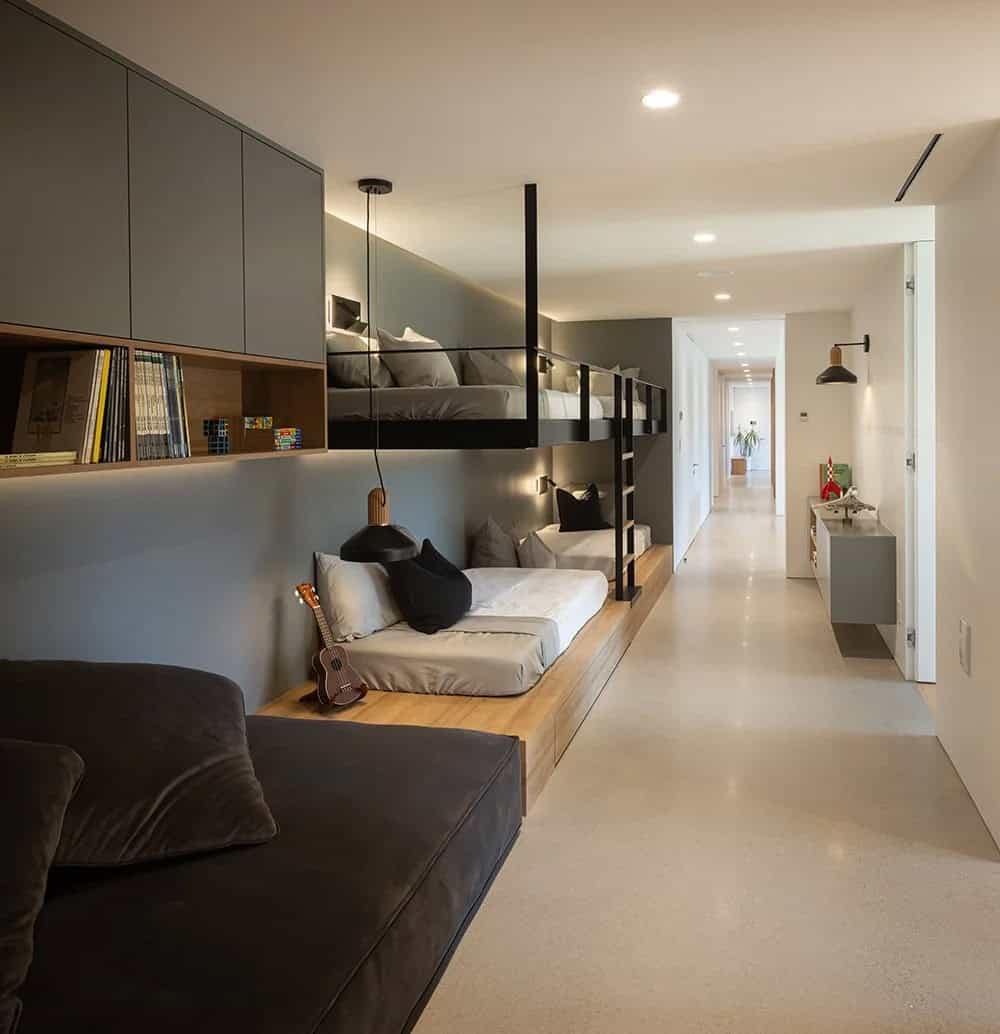 Kids bunkroom with steel and wood bunk beds, built-in grey cabinetry, open shelving, and hallway beyond