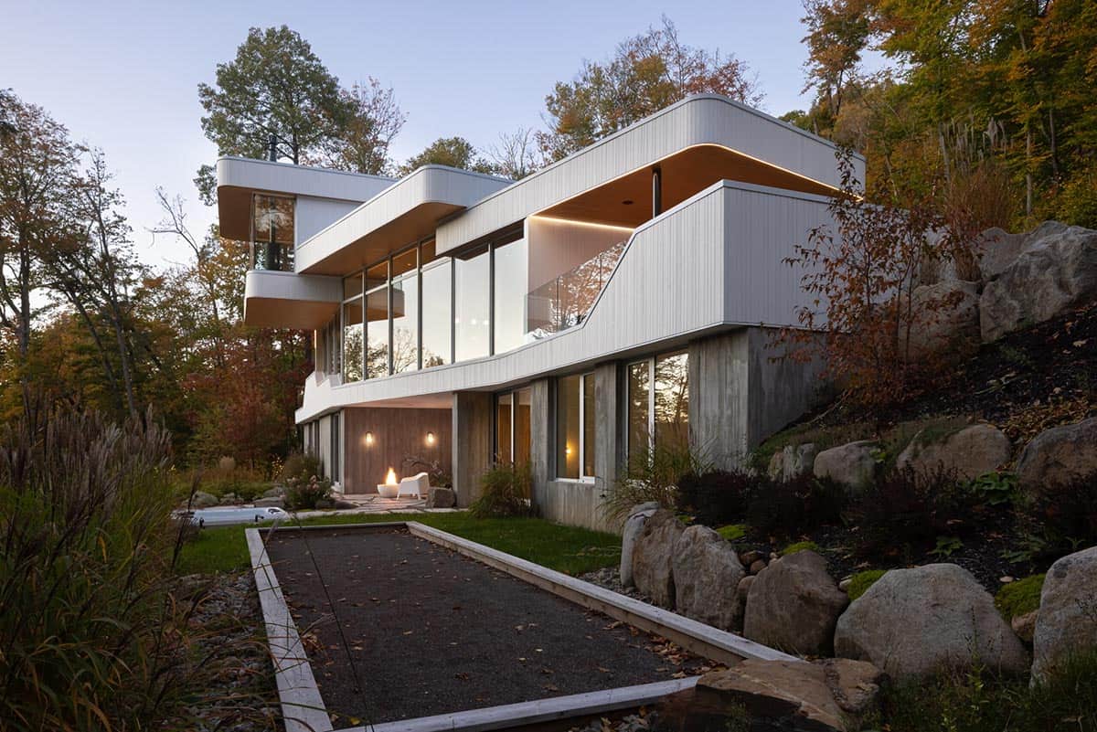 Twilight view of multi-story contemporary home with cantilevered rooflines, bocce court, and rocky landscaping
