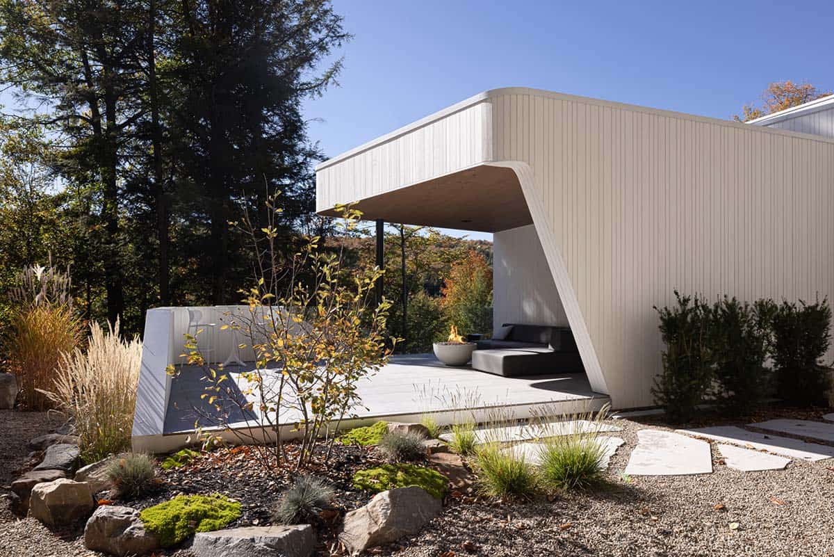 Daytime view of angled covered outdoor terrace with fire bowl, chaise lounge, and native garden plantings