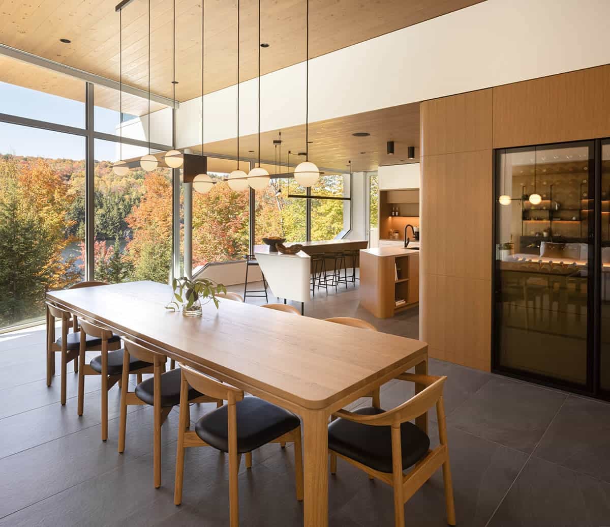 Dining room with oak table, globe pendant lights, glass-enclosed wine display, and panoramic autumn lake views