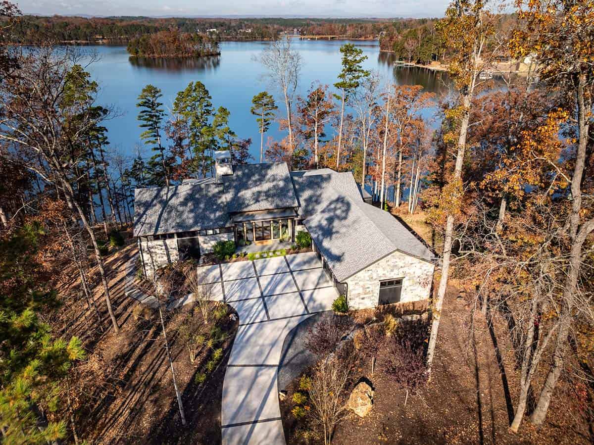 Aerial view of contemporary stone house on wooded lakefront lot