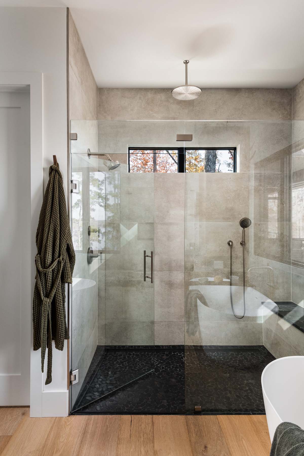 Glass-enclosed shower with concrete-look tile and freestanding tub