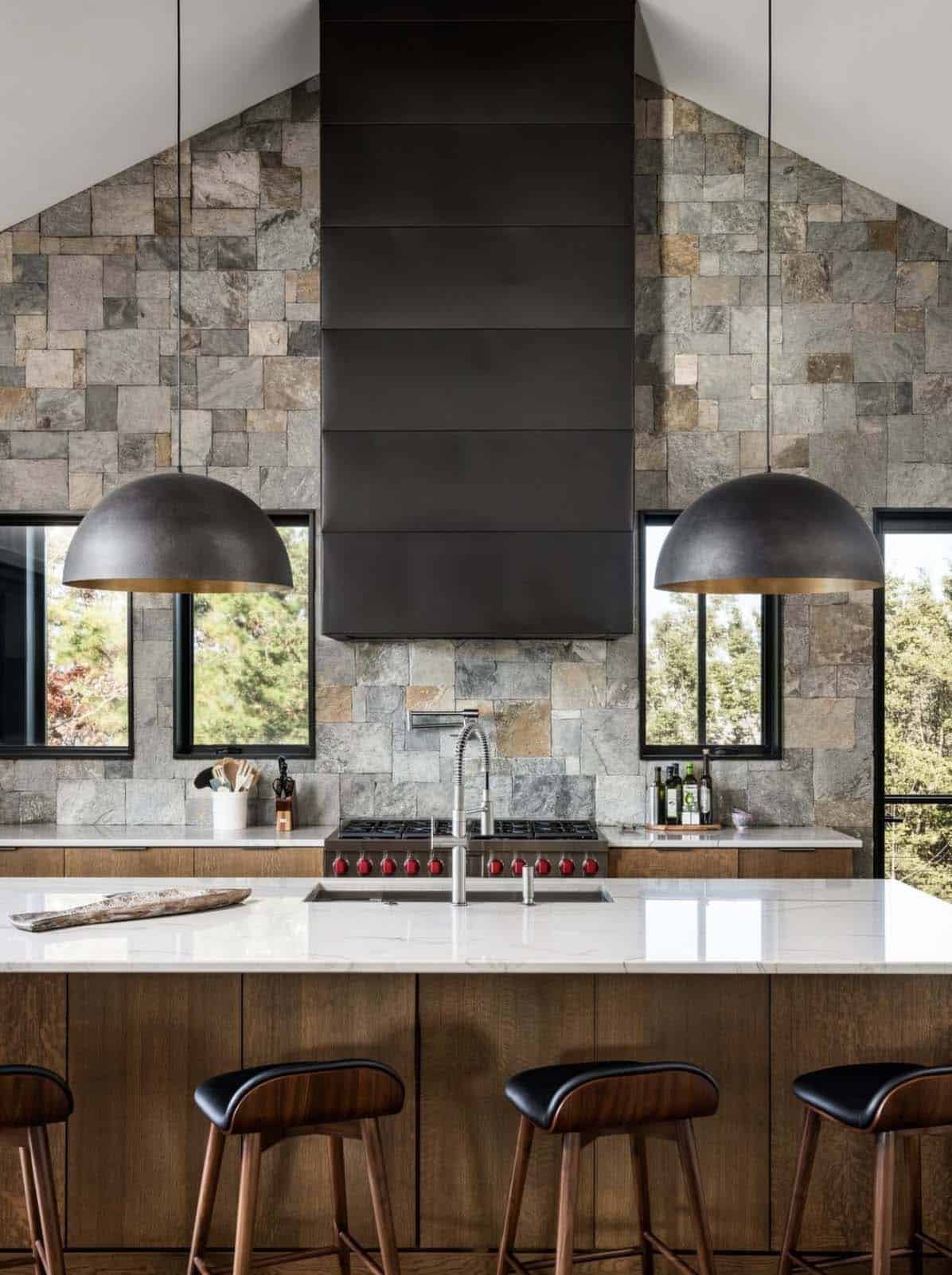 Kitchen island with marble countertop facing stone wall and black range hood