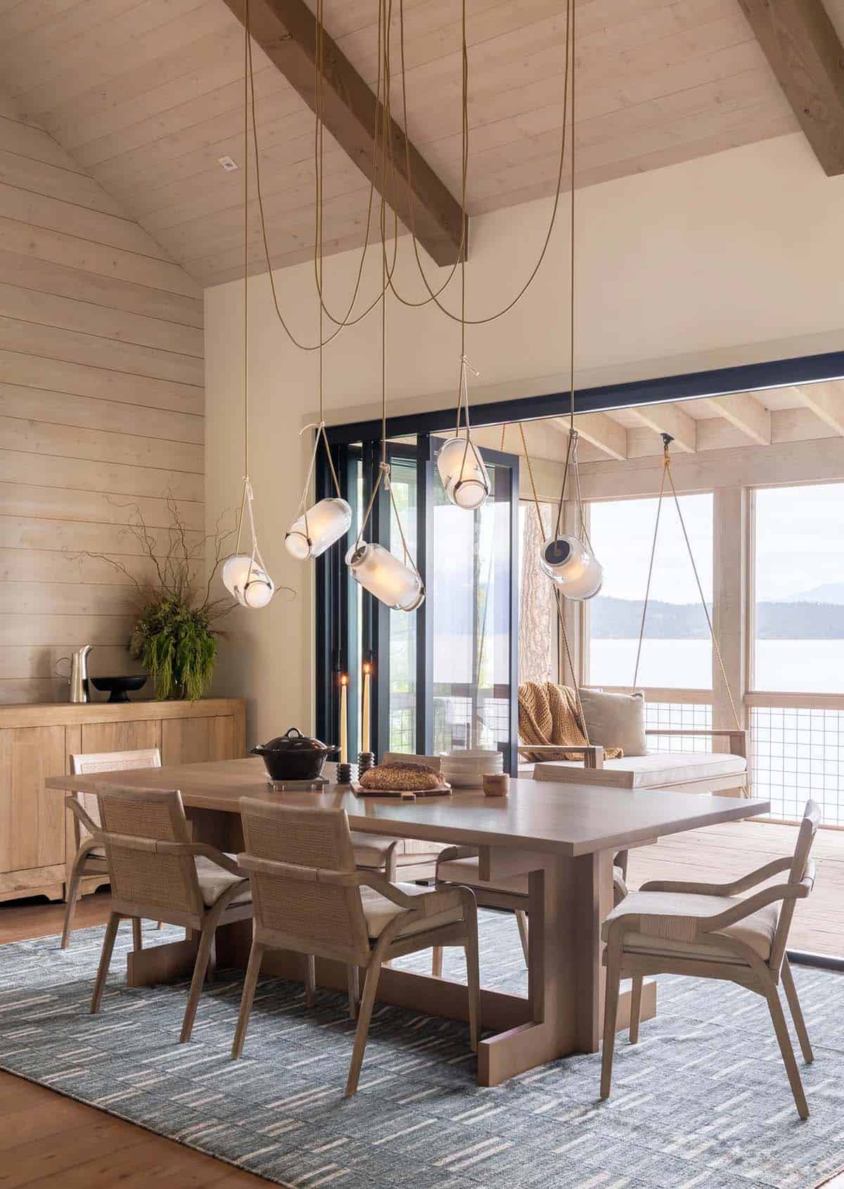 Dining table with hanging glass pendant lights over lake-view deck