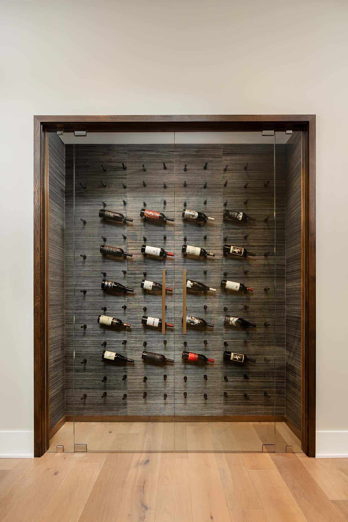 Glass-enclosed wine cellar with wall-mounted bottle pegs and dark textured panels, framed in walnut