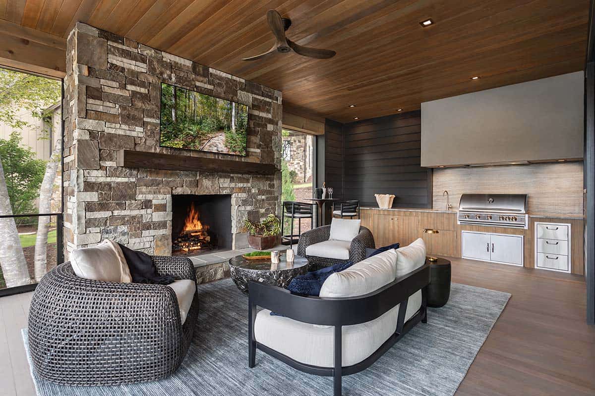 Covered outdoor living area with stacked stone fireplace, wicker seating, and built-in kitchen with grill