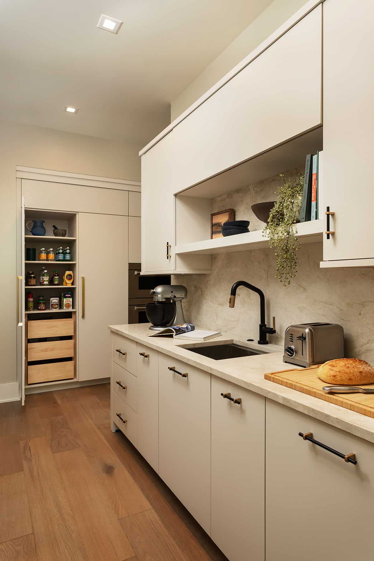 Scullery kitchen with cream cabinetry, black faucet, marble backsplash, and open pantry with pull-out drawers