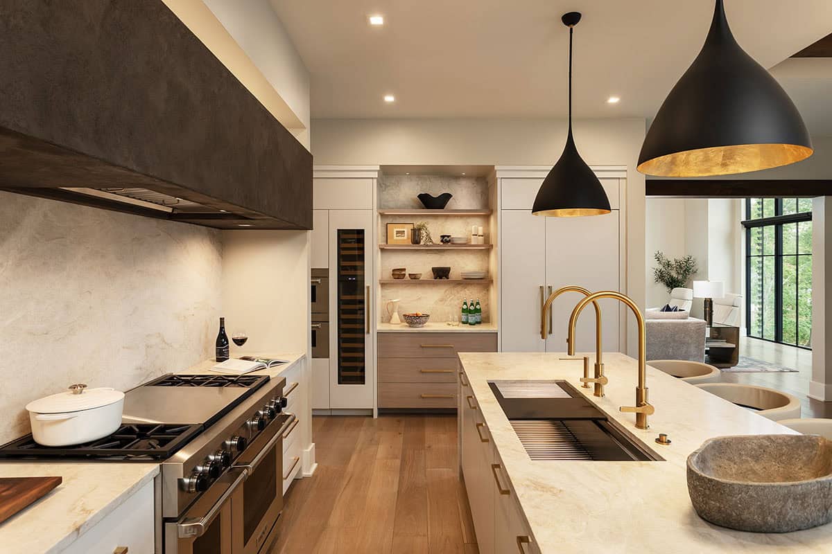 Chef's kitchen with gold faucets, dark range hood, marble island, and black pendant lights with gold interiors