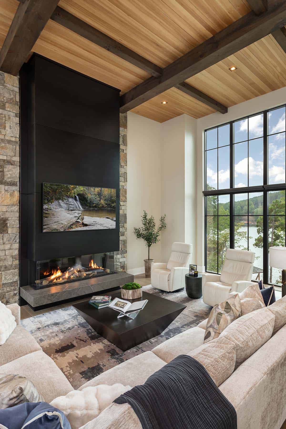 Living room featuring a tall black steel fireplace surround, wood plank ceiling, and multi-panel lake-view windows