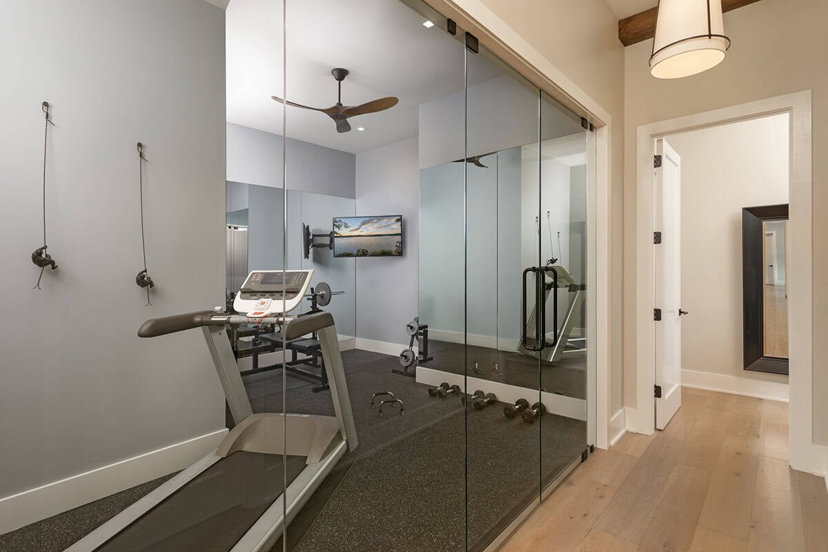 Home gym with glass sliding doors, treadmill, weight equipment, mirrored wall, and ceiling fan