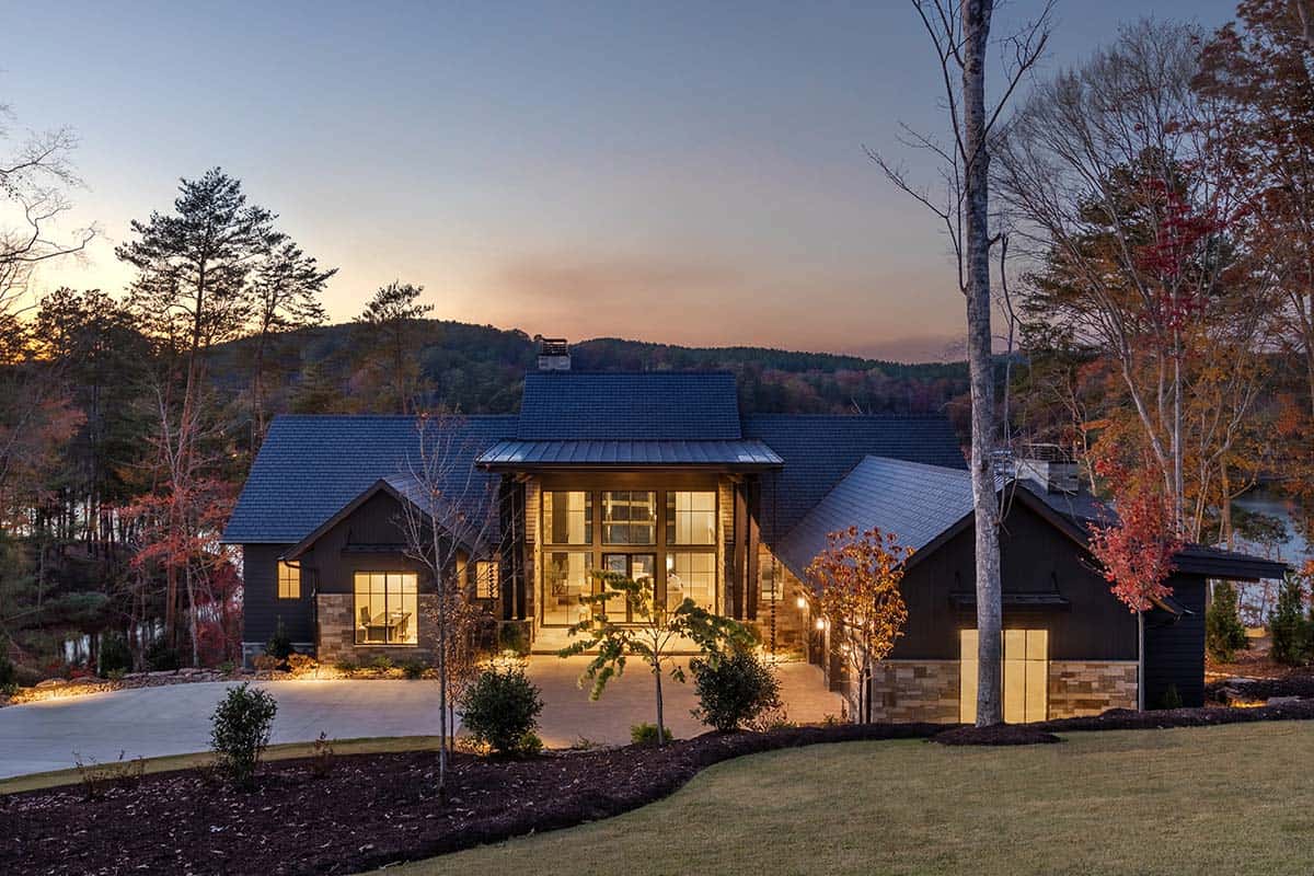 Contemporary lake house exterior at dusk with dark siding, stone accents, and glowing interior windows