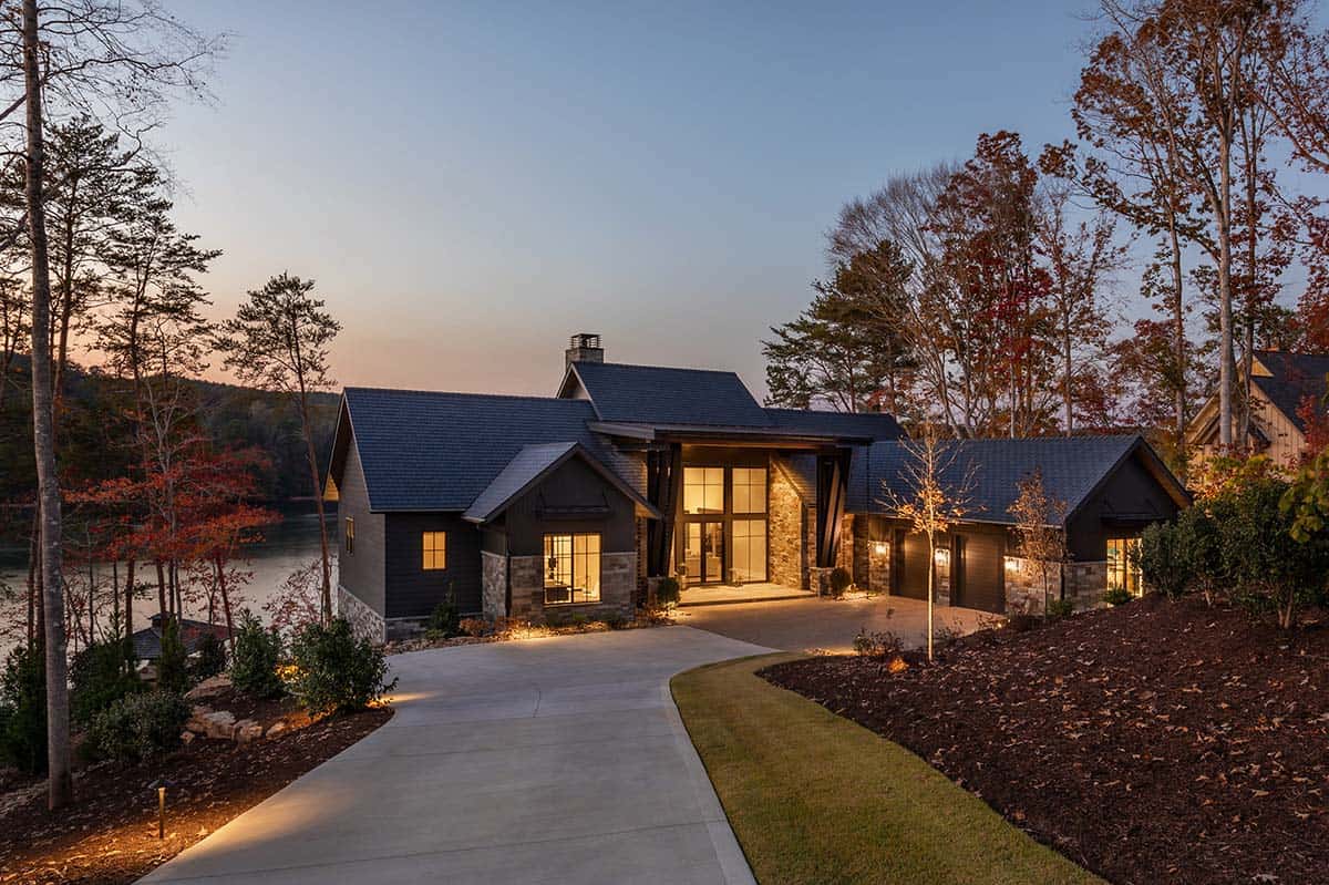 Dusk view of lake house with curved driveway, dark exterior, and stone entry tower