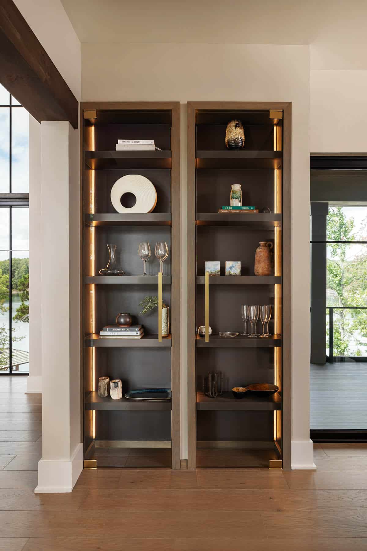Pair of built-in dark bookshelves with brass strip lighting, styled with books, glassware, and decorative objects