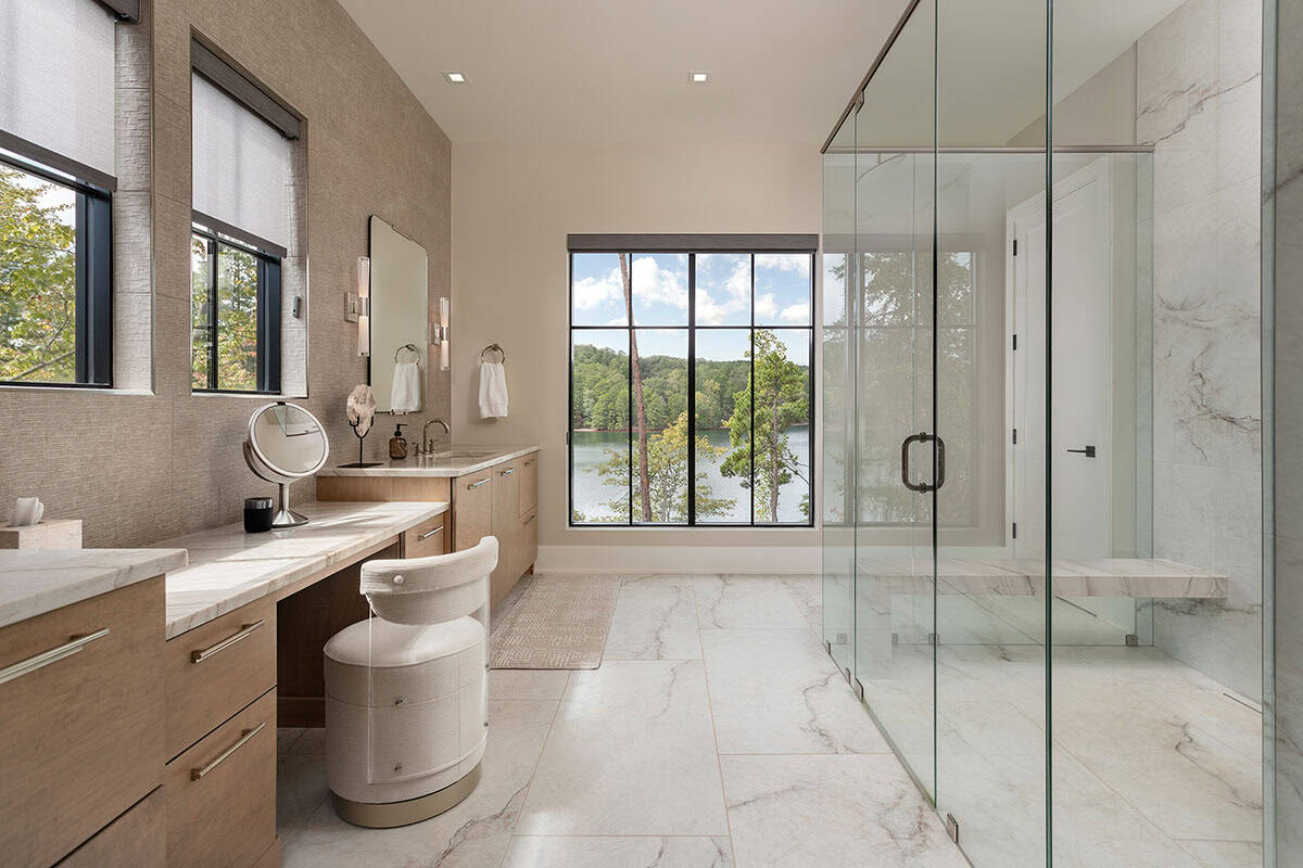 Primary bathroom with marble floors, glass walk-in shower, lake view window, and warm wood vanity