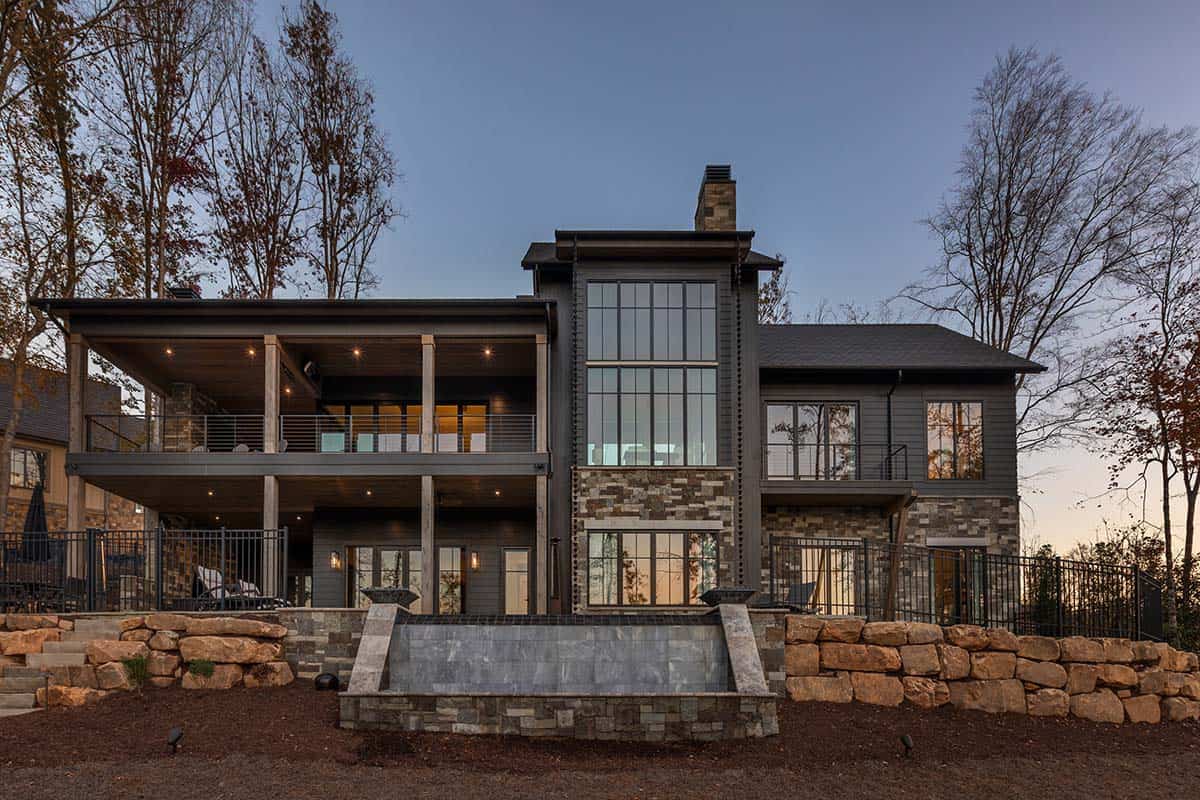 Back of lake house at twilight showing two-story glass tower, covered porch, stone facade, and terraced landscaping