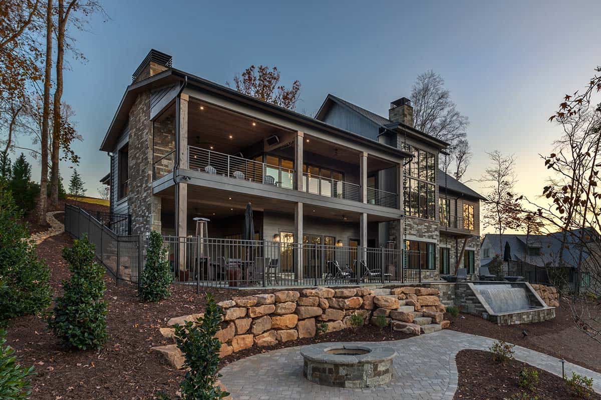 Daytime rear exterior of lake house with double-level decks, stone retaining wall, water feature, and circular fire pit