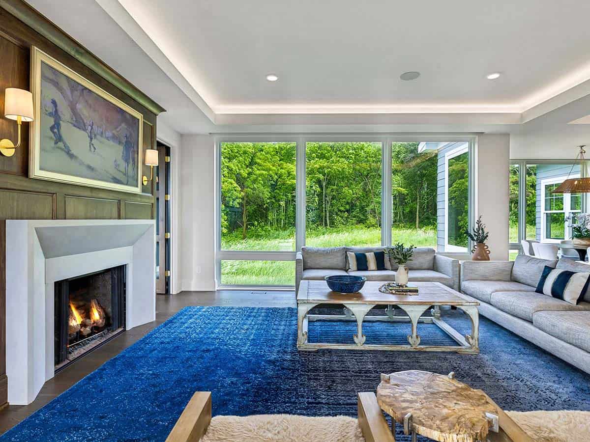 Living room with blue area rug and wall of windows overlooking woods