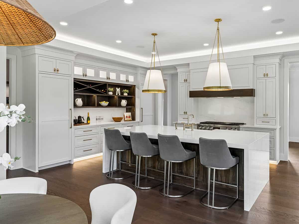 Kitchen island with gray bar stools and dark wood-front pantry shelving