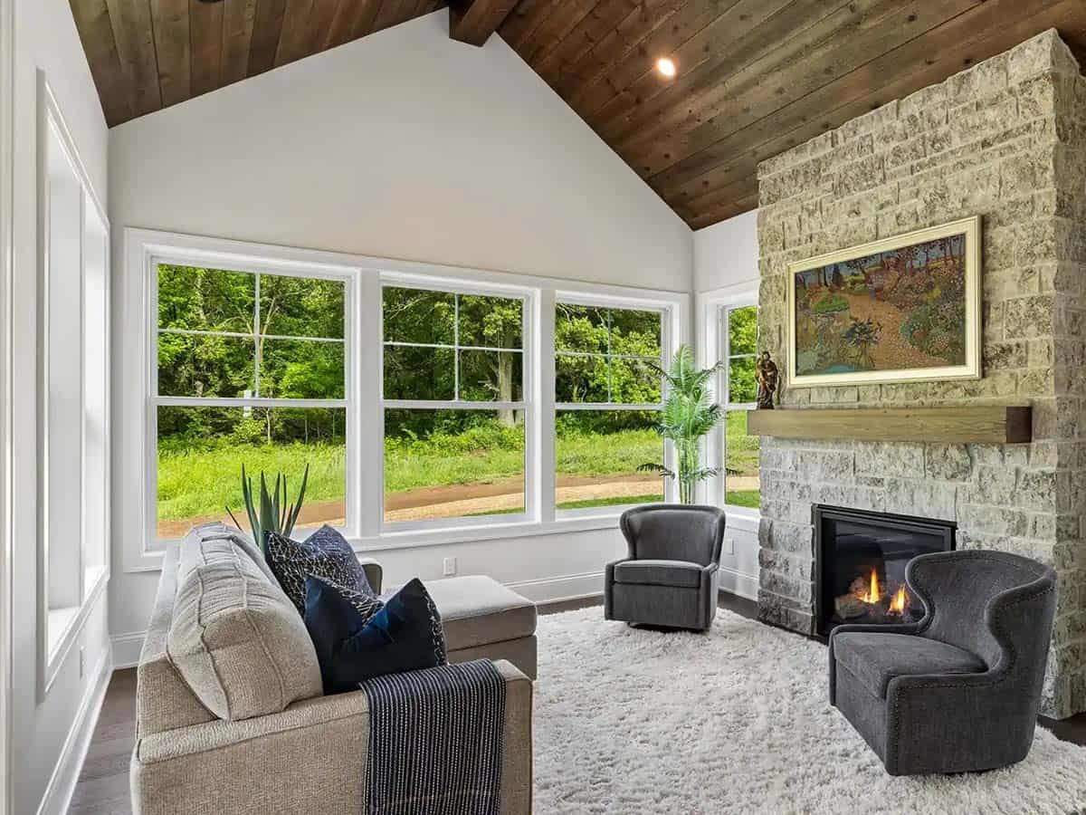 Sunroom with stone fireplace, vaulted wood ceiling, and gray armchairs