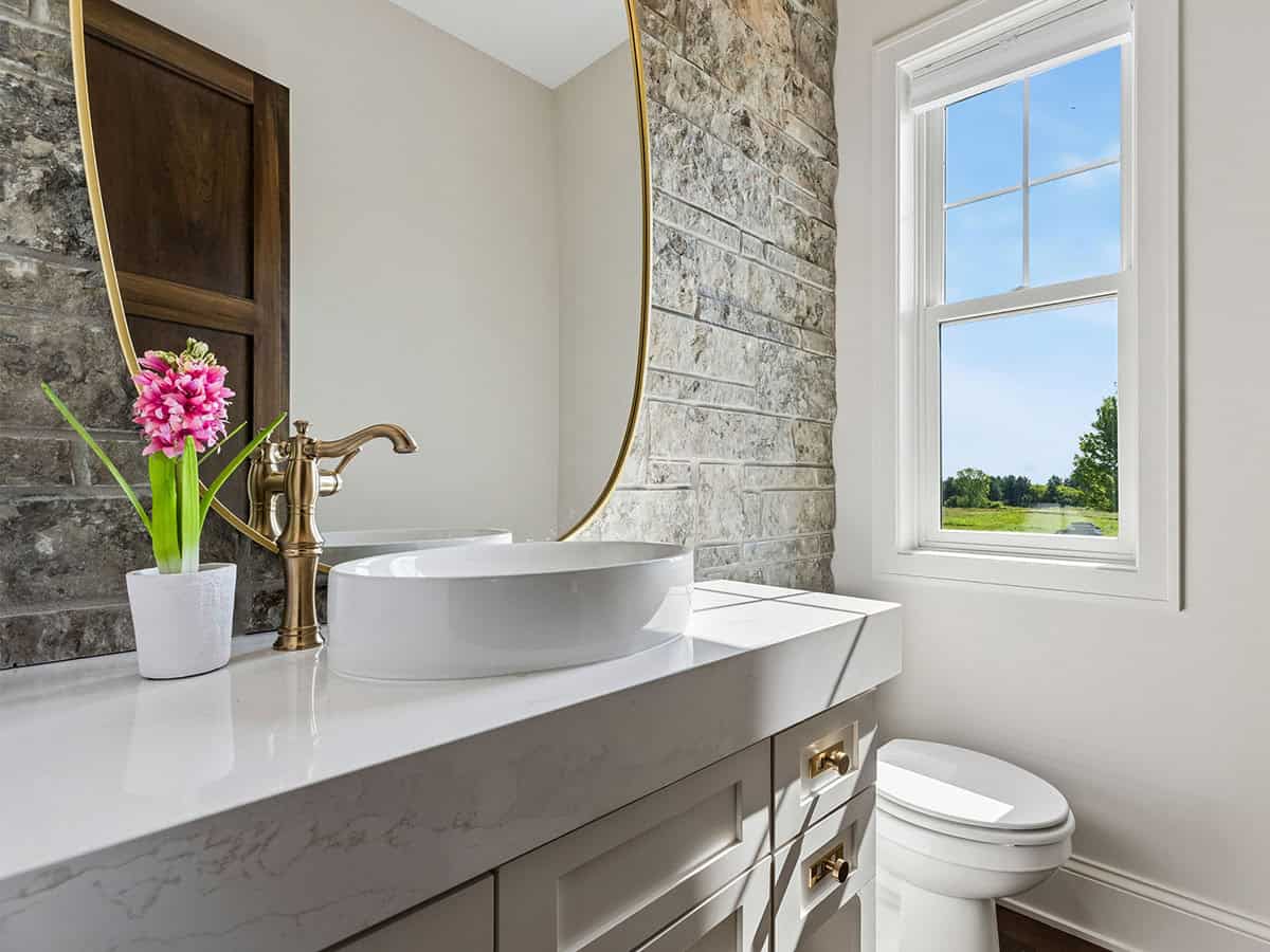 Powder room with vessel sink, stone accent wall, and brass faucet