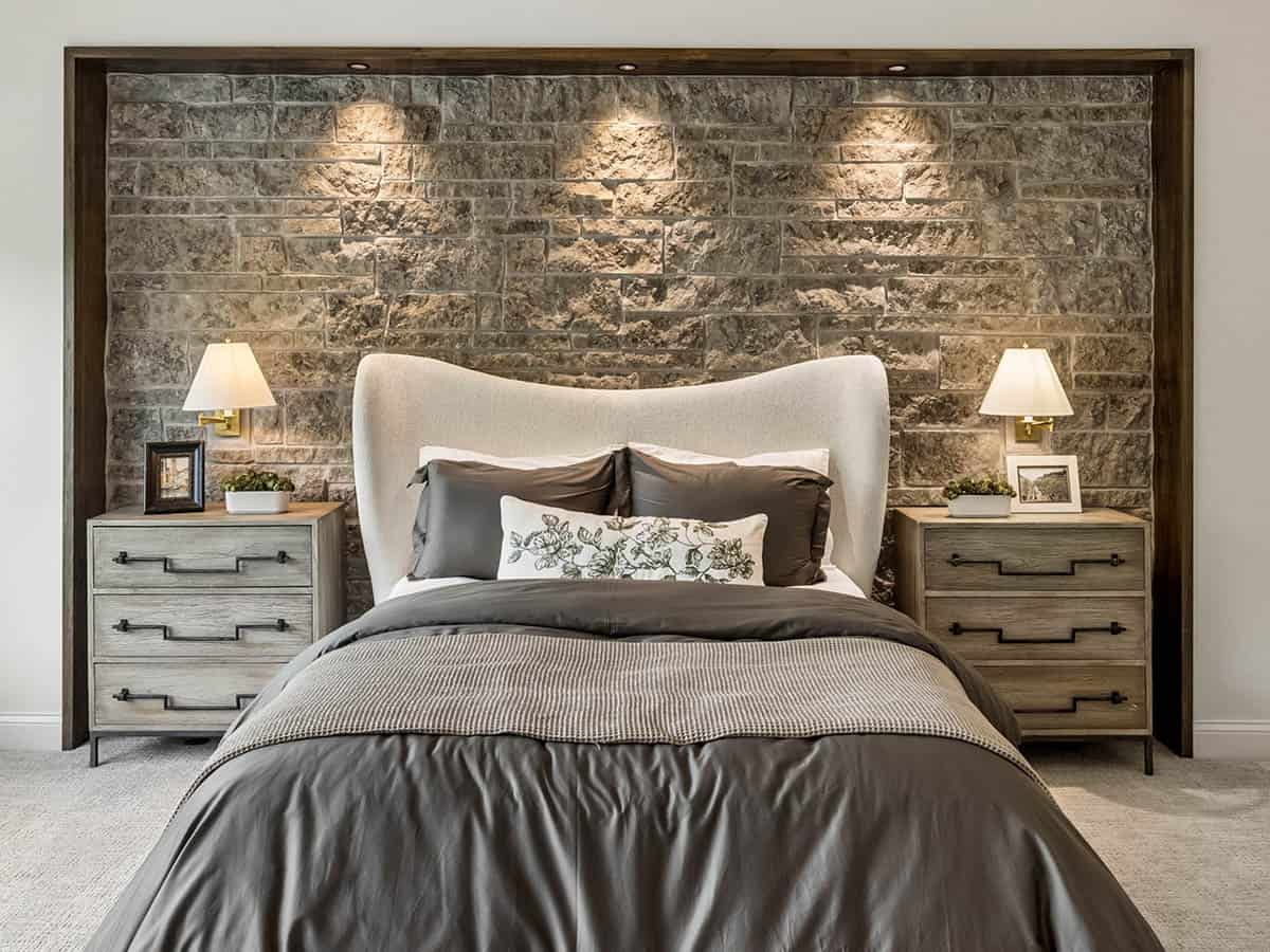 Primary bedroom bed flanked by nightstands against stone accent wall
