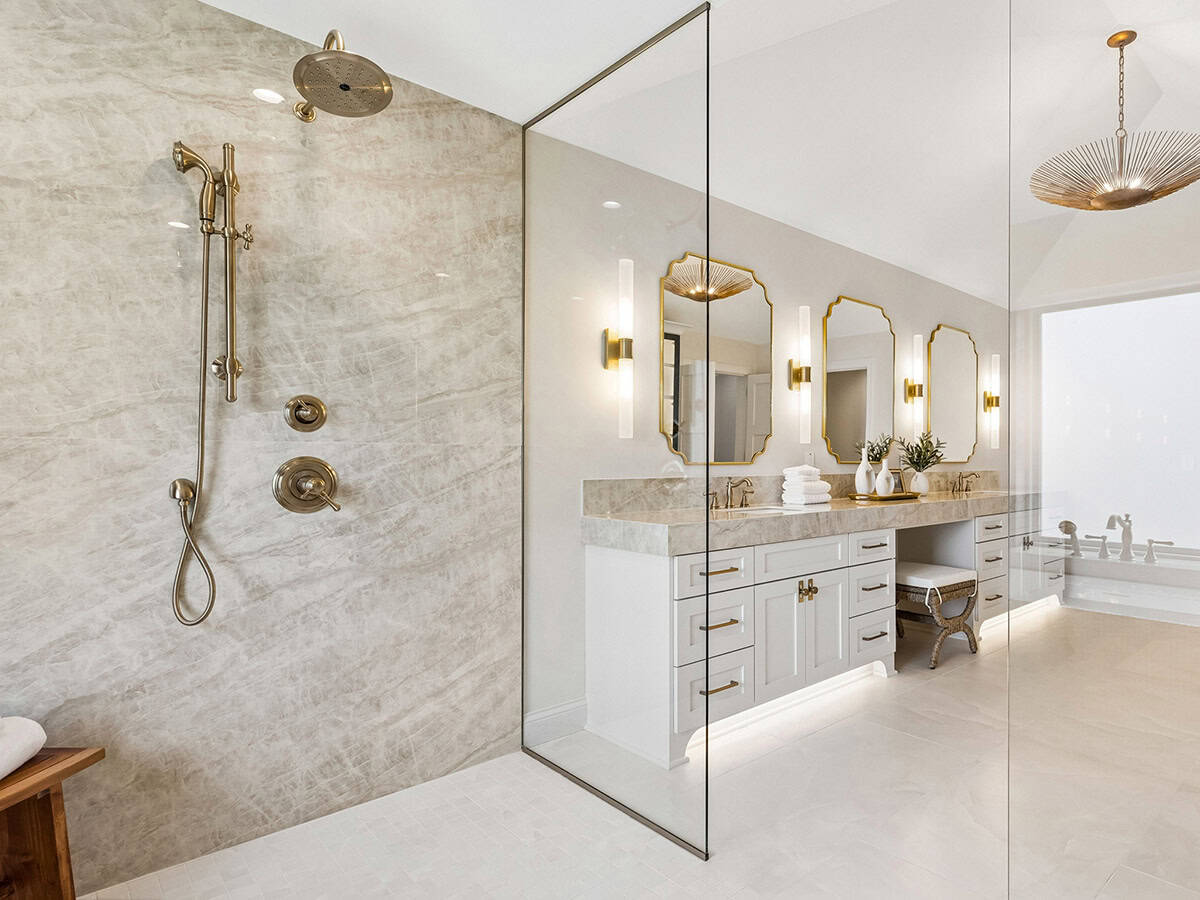 Walk-in shower with brass fixtures and marble vanity beyond