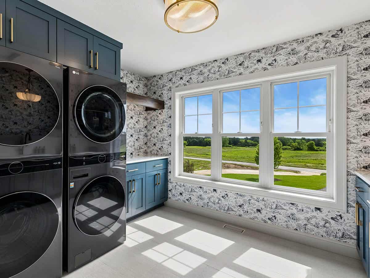 Laundry room with stacked black washer-dryer and toile wallpaper