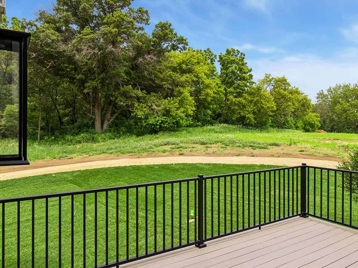 View from deck railing overlooking lawn and wooded tree line
