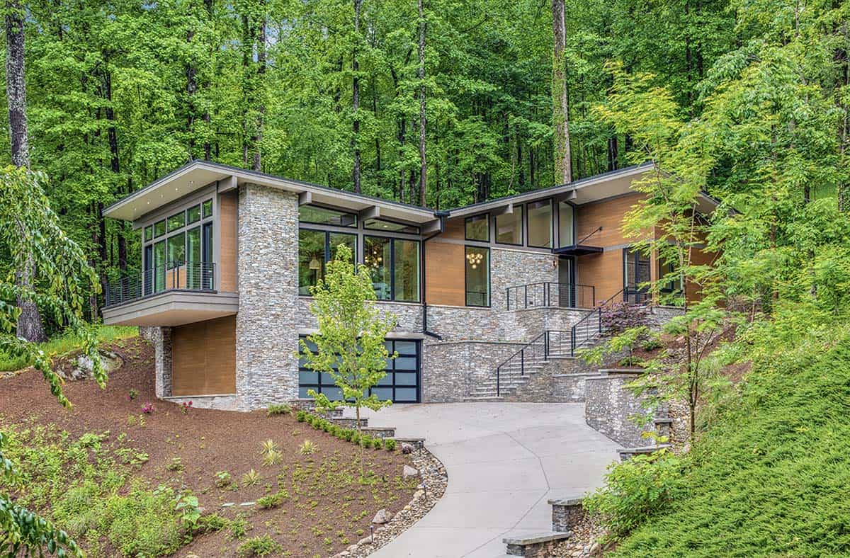 Exterior view of a contemporary mountain home with stone and wood siding, surrounded by lush green forest