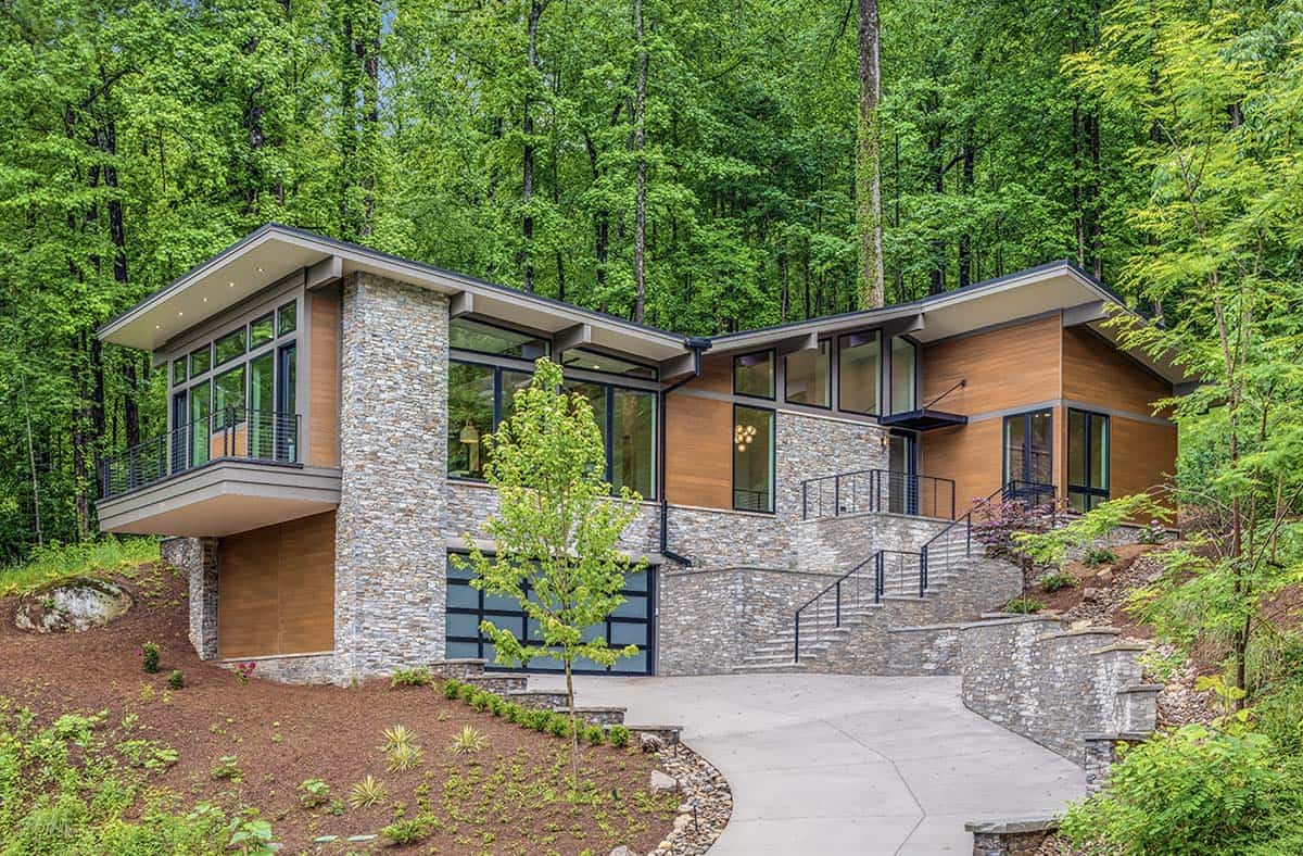 Front exterior of a modern stone-and-wood mountain house with a curved driveway and angled rooflines