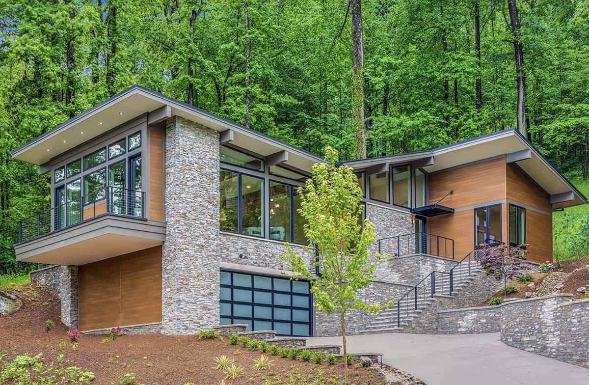 Wide exterior shot of the contemporary home showing stacked stone base, wood paneling, and a cantilevered balcony