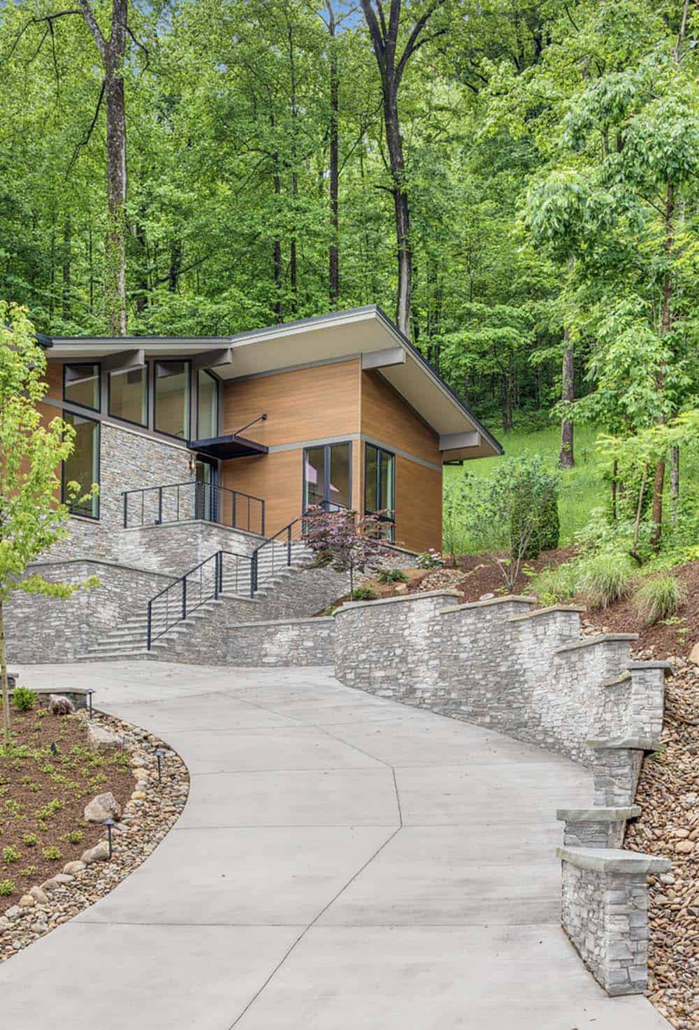Walkway leading to the home's entrance, lined with stone retaining walls and surrounded by forest