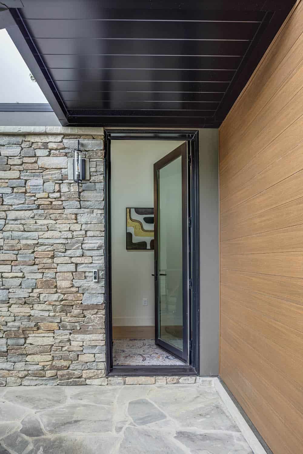 Close-up of the front entry with open glass door, stone wall, and wood paneling