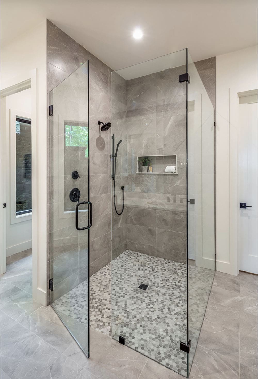 Modern glass-enclosed walk-in shower with gray stone tile and hexagon mosaic floor