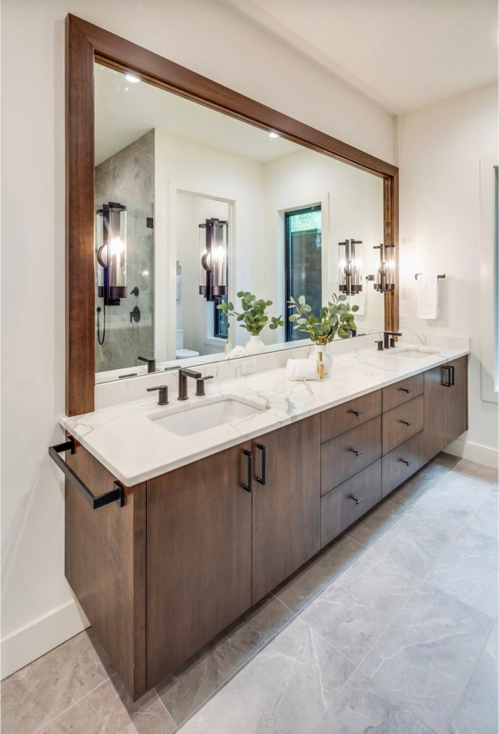 Bathroom vanity with dark wood cabinetry, marble countertop, and large framed mirror