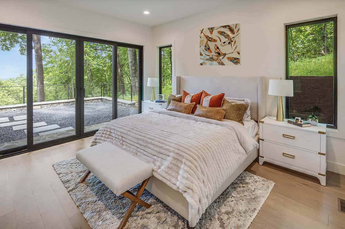 Bright bedroom with upholstered bed, sliding glass doors, and forest view
