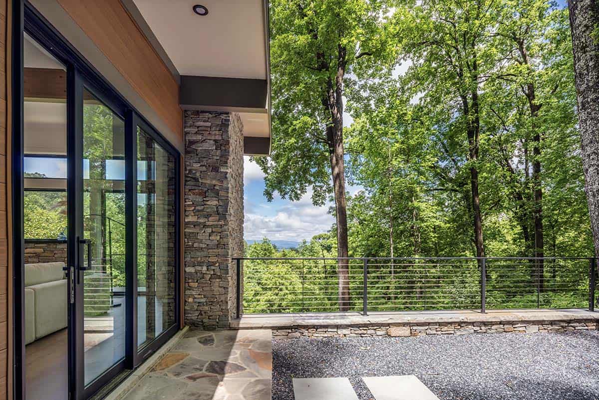 Covered patio with stone column, glass doors, and panoramic mountain forest view
