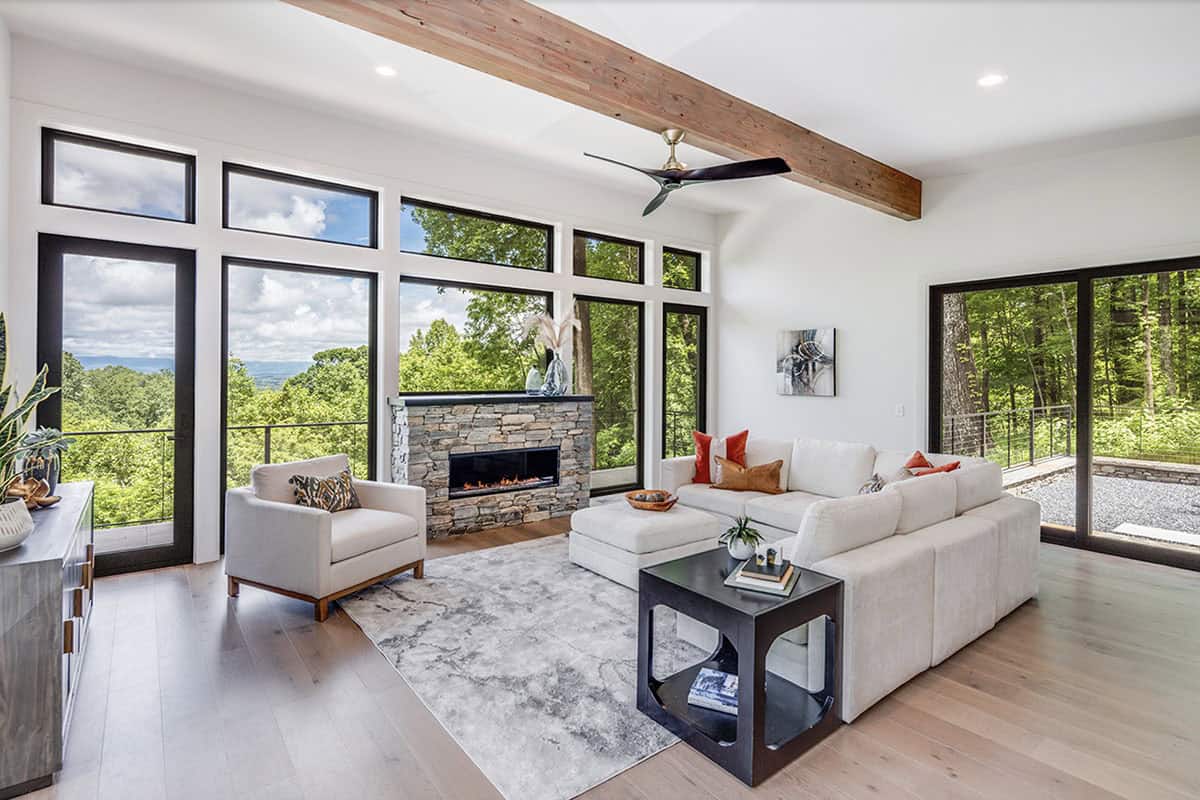 Living room with white sectional sofa, stone fireplace, and wraparound windows
