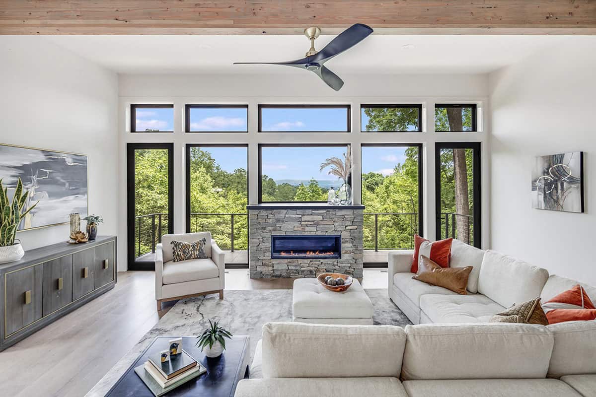 Living room with sectional sofa, ceiling fan, and stone fireplace framed by large windows